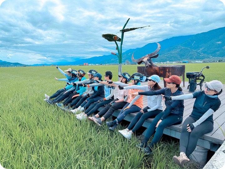 車友們坐在稻田邊的木棧道上一起伸手指向遠方